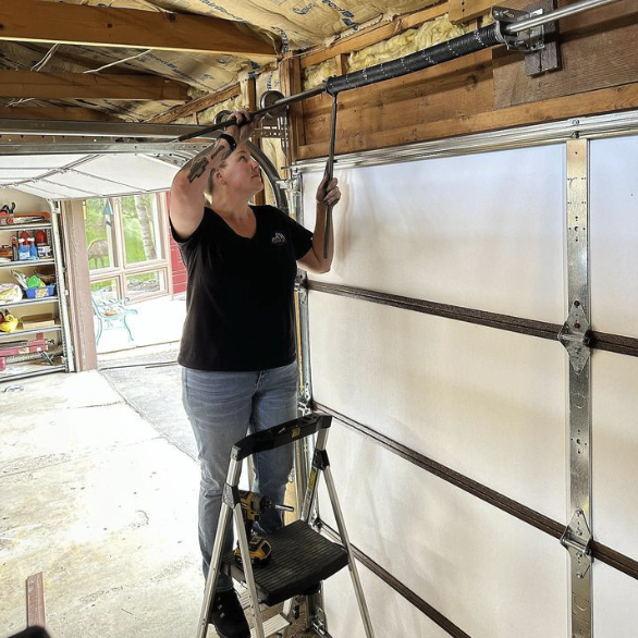 Woman repairing garage door spring on ladder.
